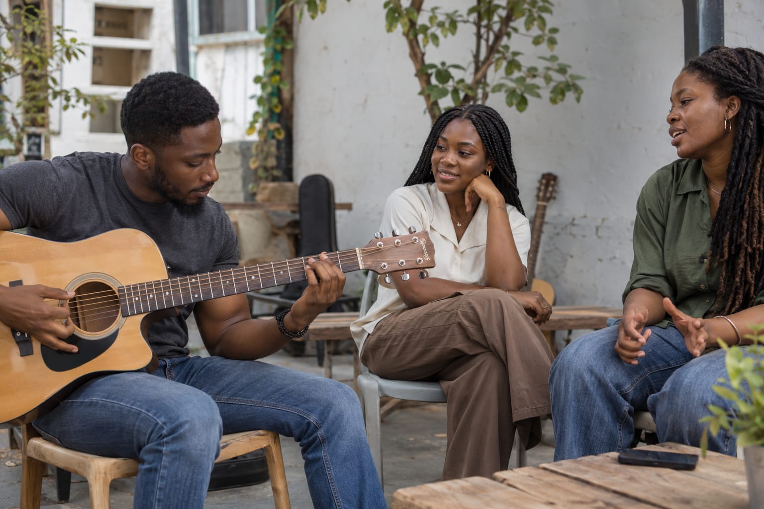 Three young adults sharing a relaxed acoustic guitar session.